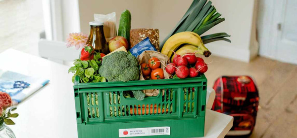 KI generiert: Eine grüne Kiste voller frischem Obst und Gemüse auf einem Tisch. Enthält KEIN Text.