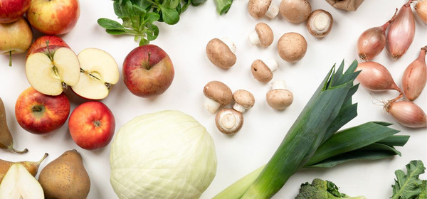 KI generiert: Verschiedene frische Obst- und Gemüsesorten liegen auf weißem Hintergrund verteilt.