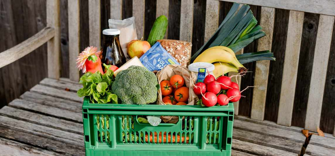 KI generiert: Eine grüne Kiste mit frischem Obst, Gemüse und Lebensmitteln auf einer Holzbank.