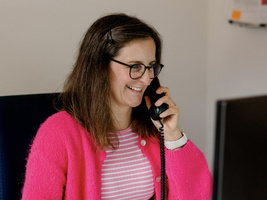 KI generiert: Eine lächelnde Person telefoniert im Büro.